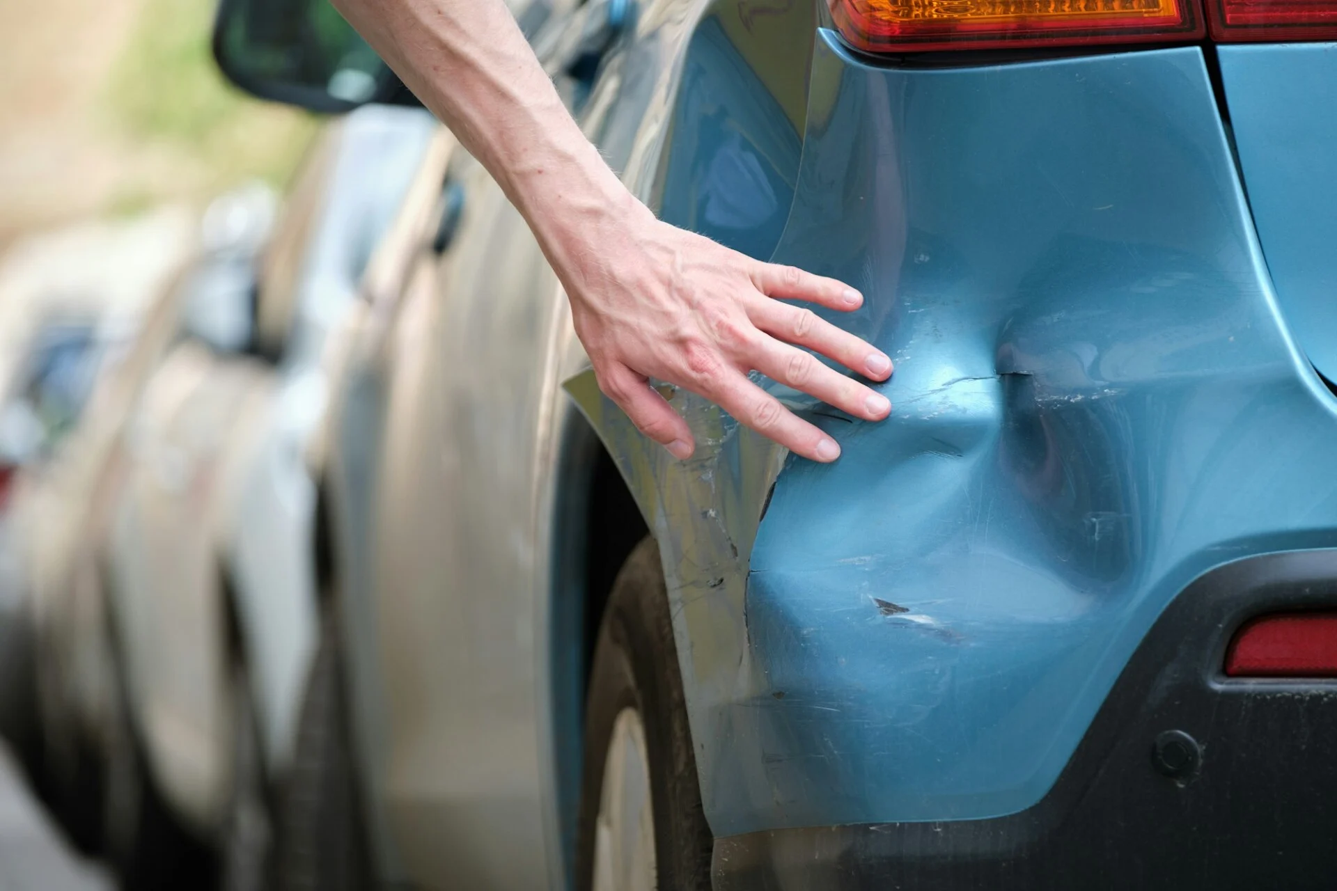 Driver hand examining dented car with damaged fender parked on city street side